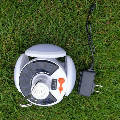 Folding LED camping light opened flat on grass with its charging cable connected; cable shown, not included.