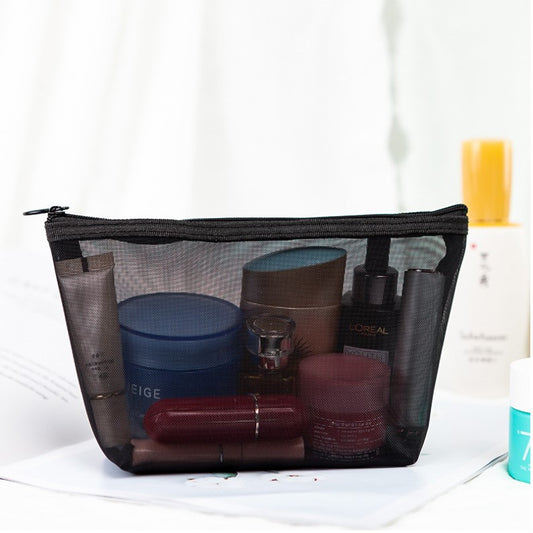 Black mesh toiletry bag packed with cosmetics on a white surface while packing for a trip; cosmetics not included.