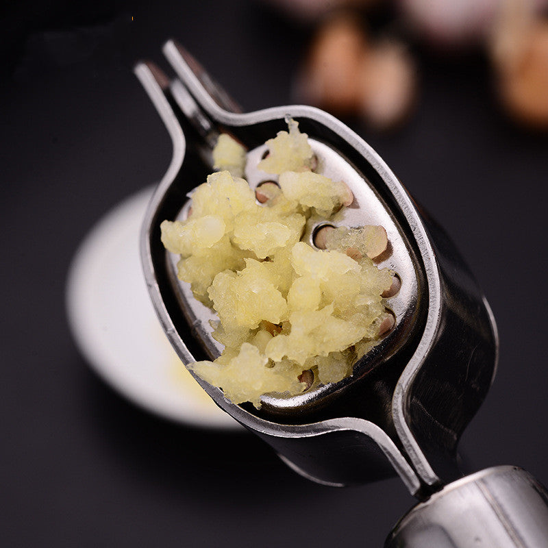 Stainless steel garlic press held over a dark surface with freshly minced garlic in its basket; garlic not included.
