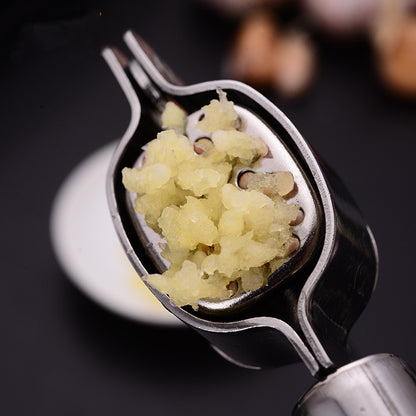Stainless steel garlic press held over a dark surface with freshly minced garlic in its basket; garlic not included.