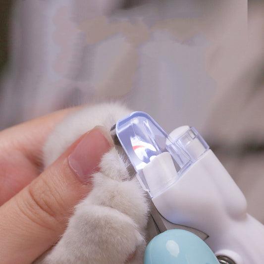 White and light blue LED pet nail clipper trimming a claw on a cat's paw held in a hand; cat and hand not included.
