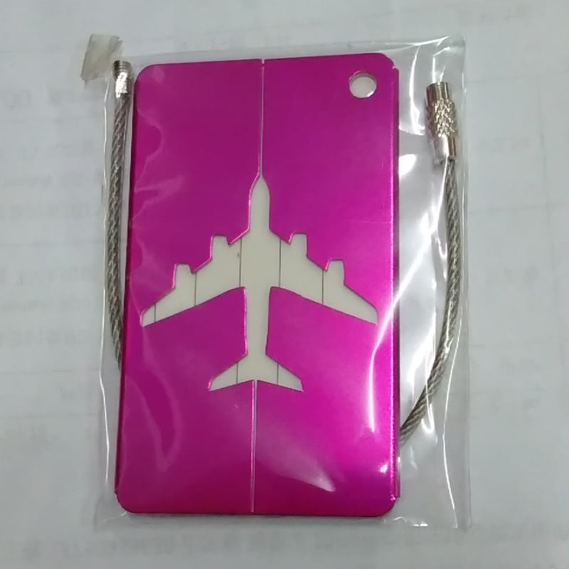Pink aluminum luggage tag with an airplane cut-out and wire loop, shown inside its clear retail packaging.