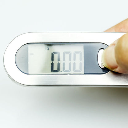 Hand holding a silver digital luggage scale against a white background while weighing a bag for a flight; hand not included.