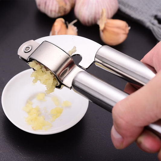 Hand squeezing a stainless steel garlic press into a small white dish on a kitchen counter; hand and dish not included.