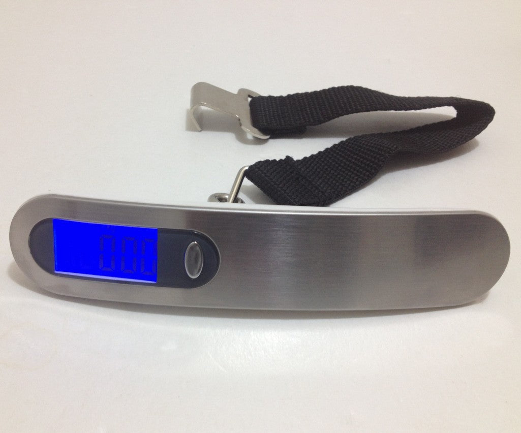Silver and black digital luggage scale lying flat on a white surface with its readout visible for a pre-flight weight check.
